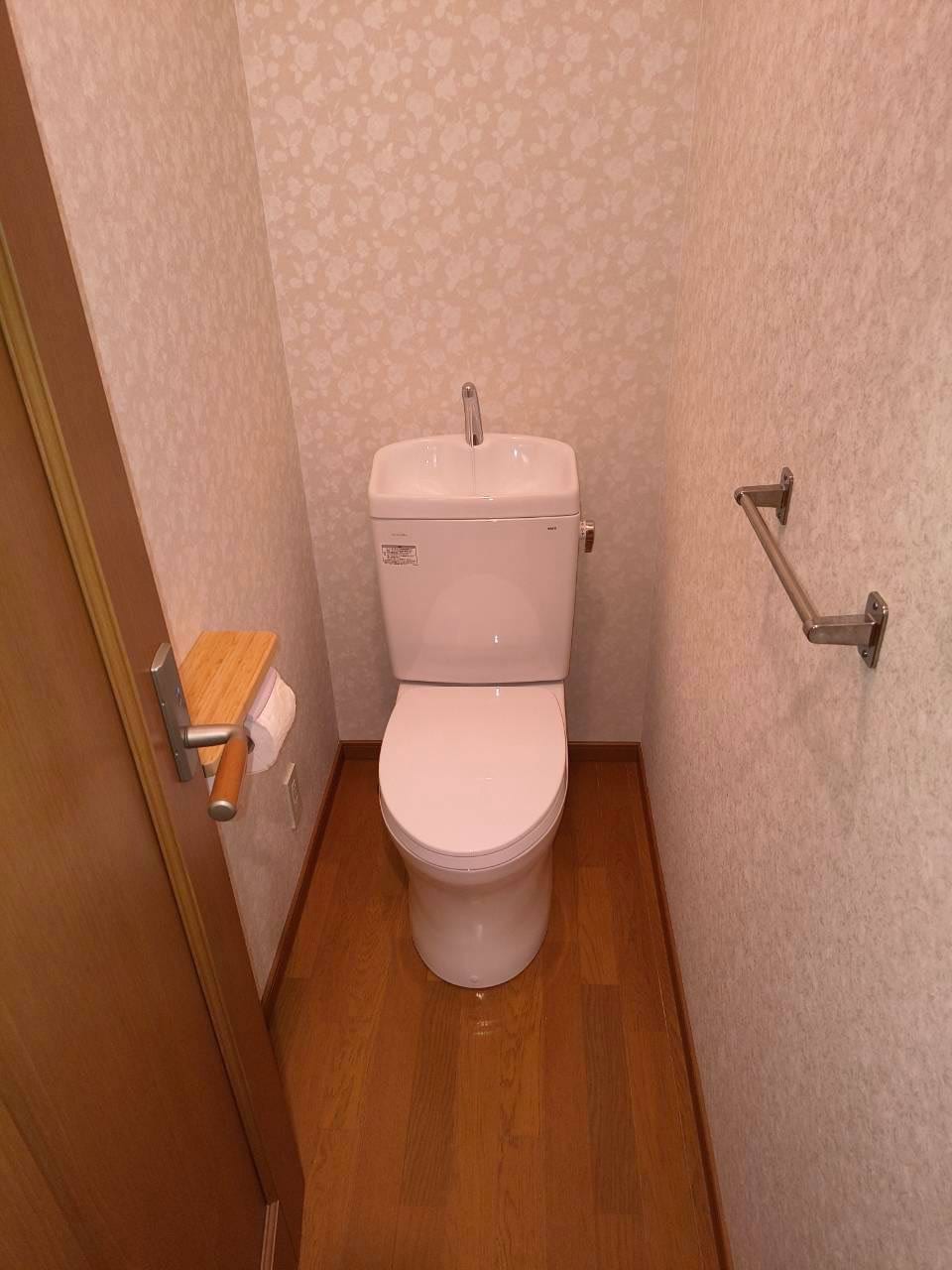 施工後のトイレ。白い新品の便器と、張り替えたクロス・クッションフロア、手すりを設置